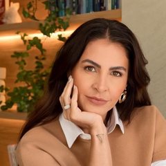 Carmem Mendes, com a mão no rosto, em frente a uma estante de livros
